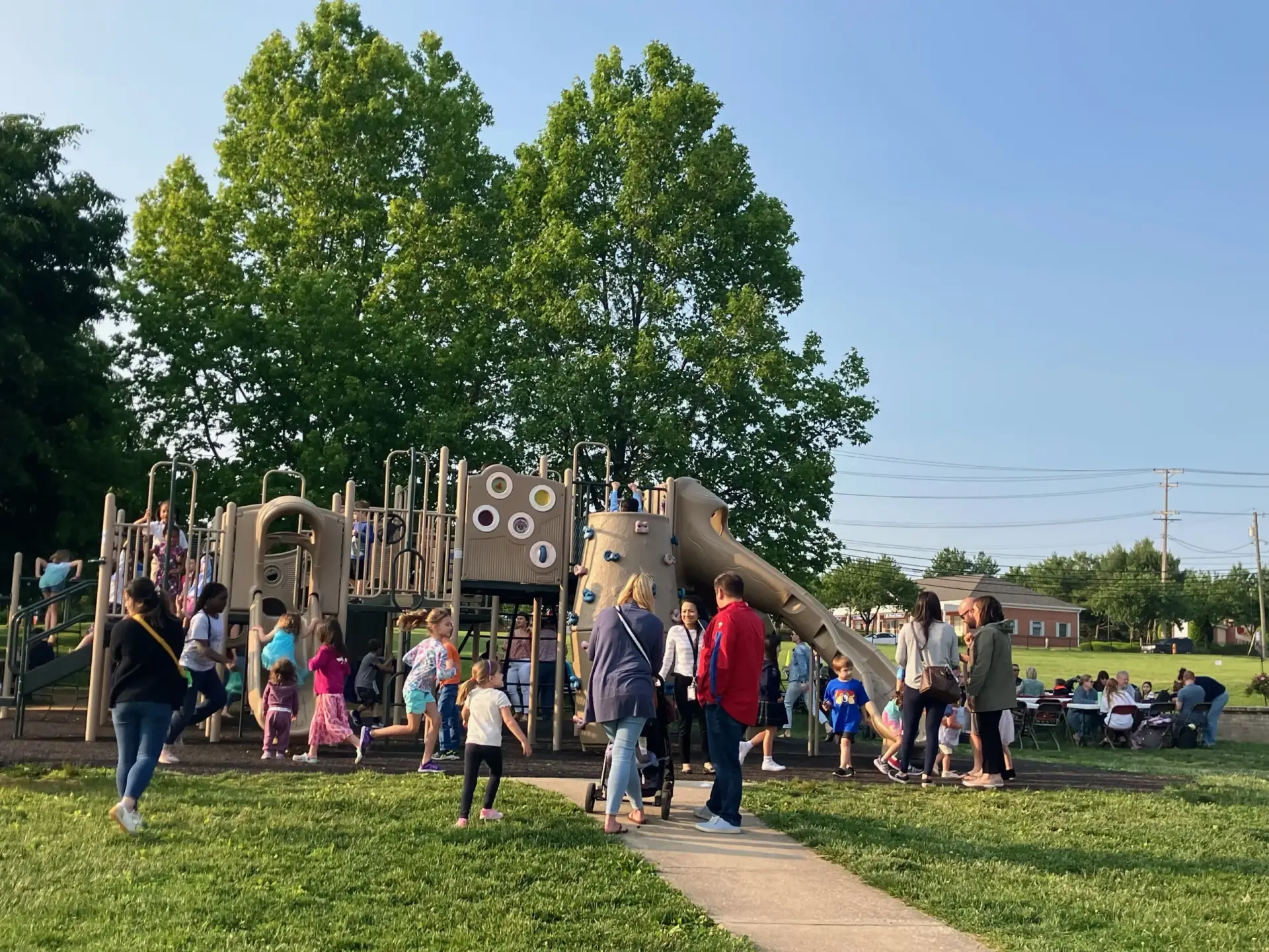 Image: St. Louis families enjoying a summer evening social on campus and kids playing on the play set.